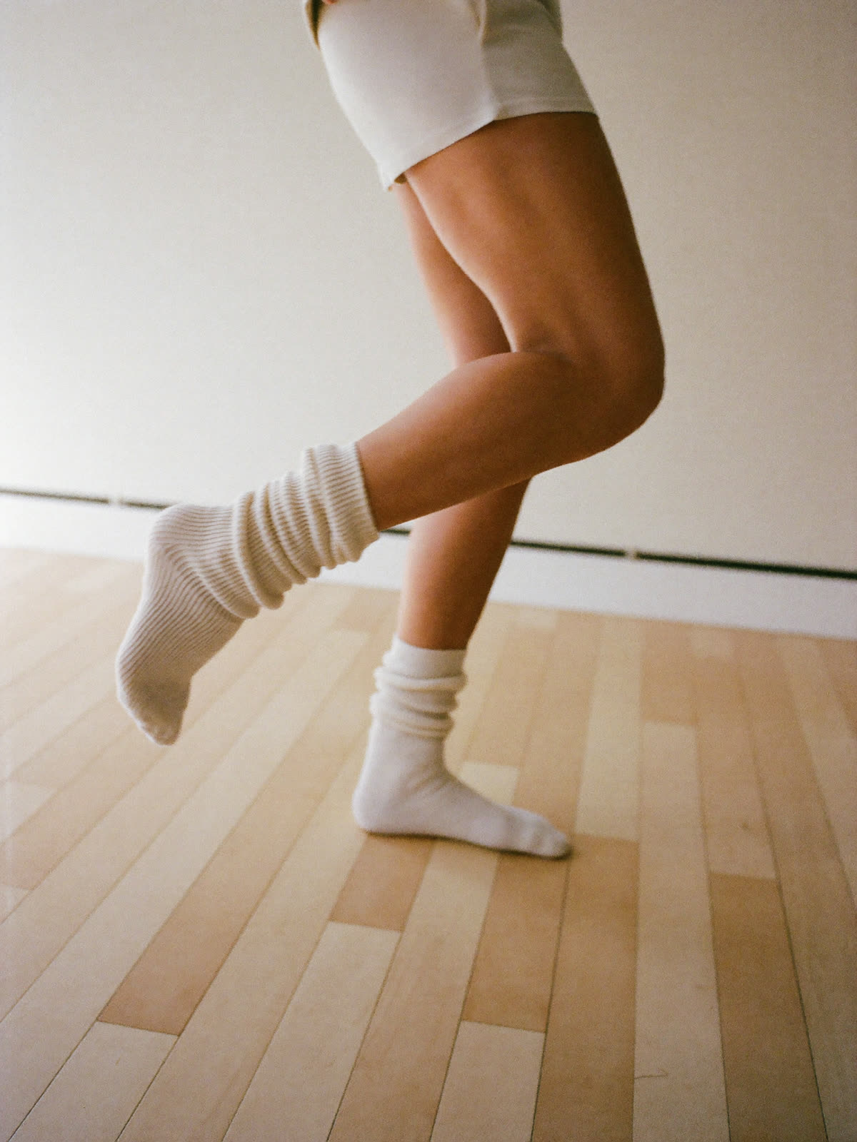 A dancer mid-step in long slouchy socks on a pale timber floor