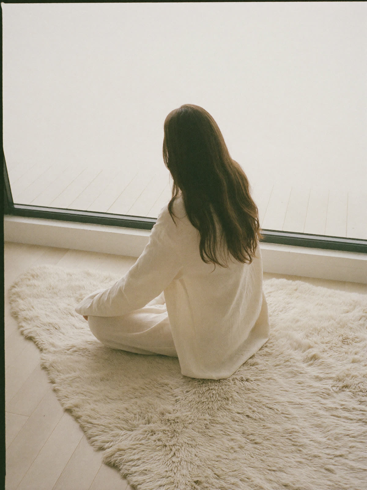 A woman seated quietly on a soft rug beside a bright window
